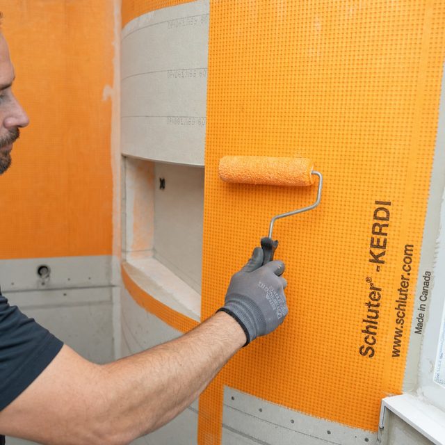 Orange waterproofing membrane rolled over a shower pan and curb