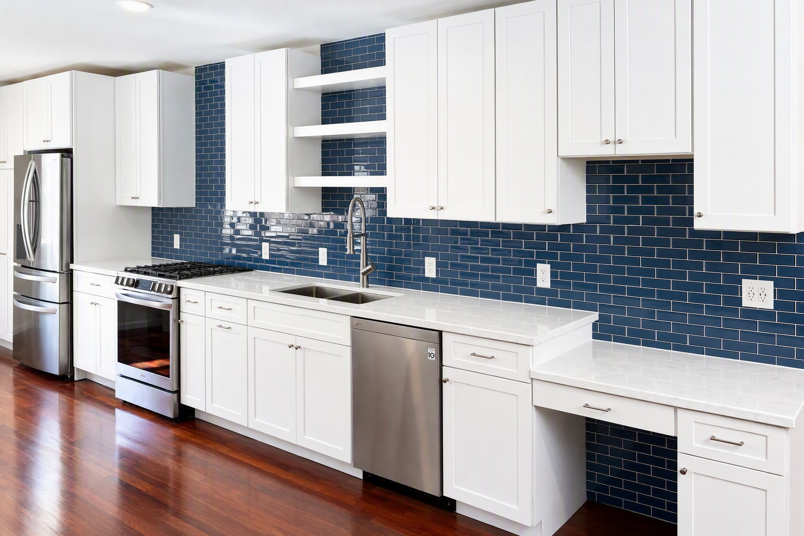 The same kitchen after — navy glass subway tile run full height behind white shaker cabinets and quartz counters