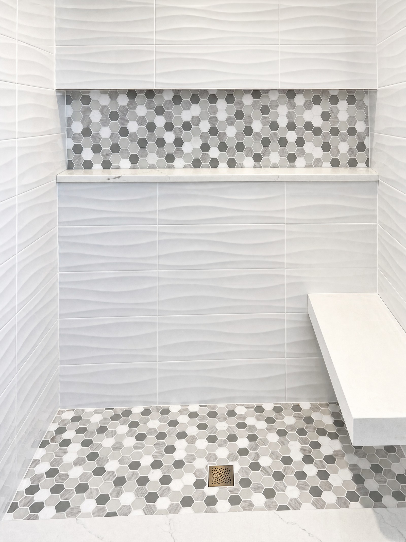 Shower in white wave-texture wall tile with a grey hexagon mosaic band, matching mosaic floor and a built-in bench