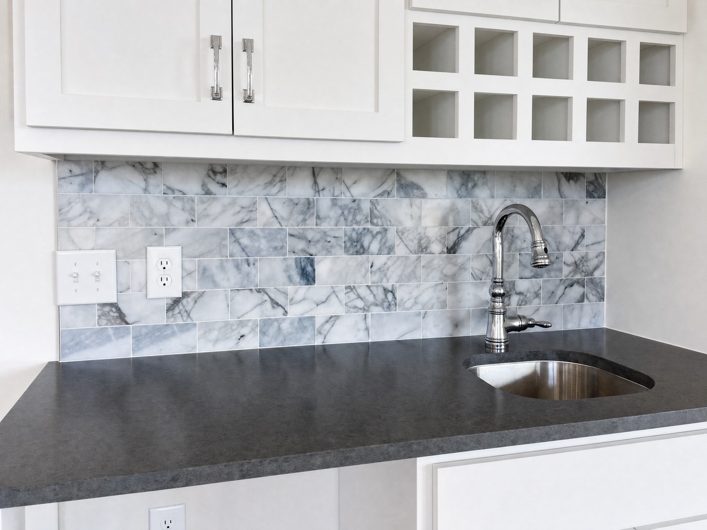 Grey and white marble mosaic backsplash above a charcoal countertop with a stainless bar sink