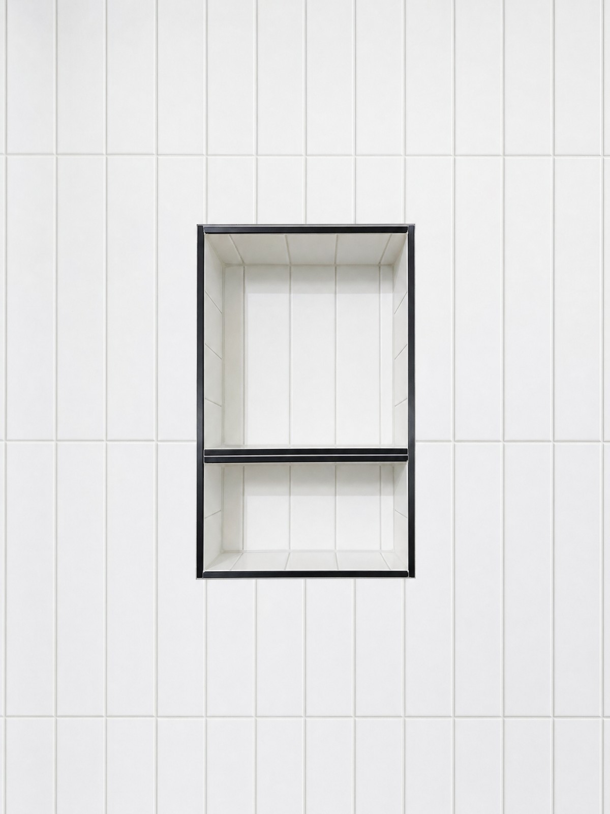 A recessed shower niche with black metal trim set into white stack-bond tile, up close