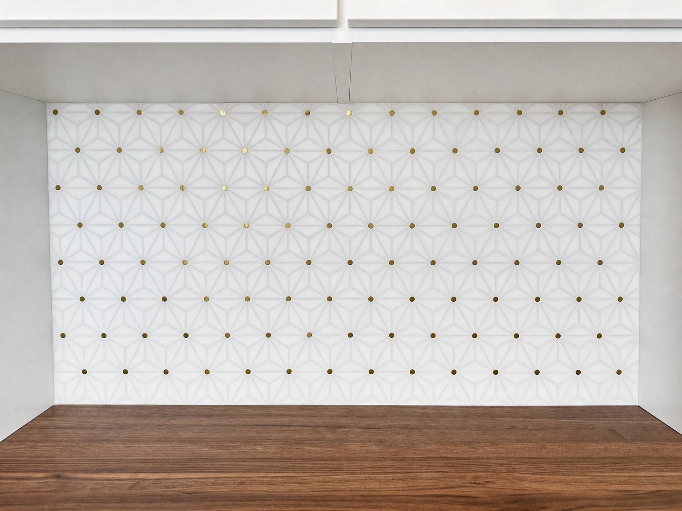 White geometric star and cross mosaic backsplash with small brass accent dots above a walnut countertop