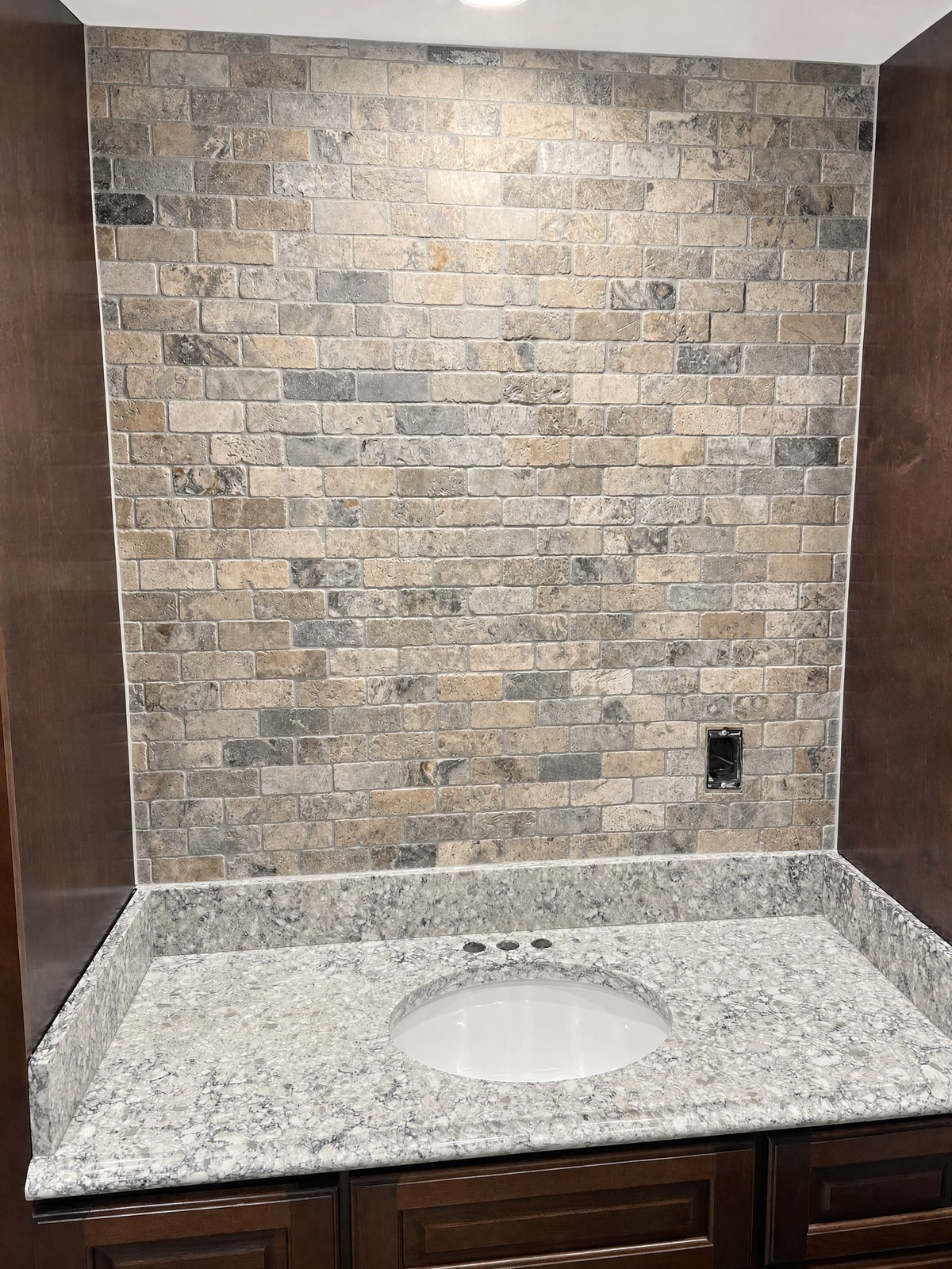 Tumbled travertine brick-pattern backsplash above a speckled granite vanity top with an oval undermount sink