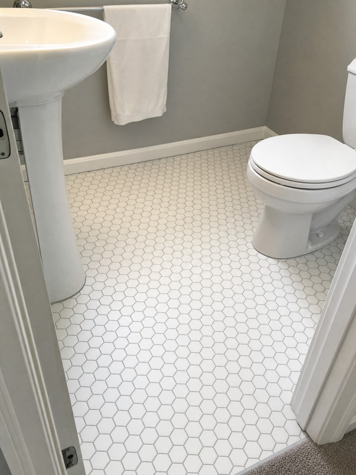 Guest bathroom floor in white hexagon mosaic tile cut cleanly around a pedestal sink and toilet base