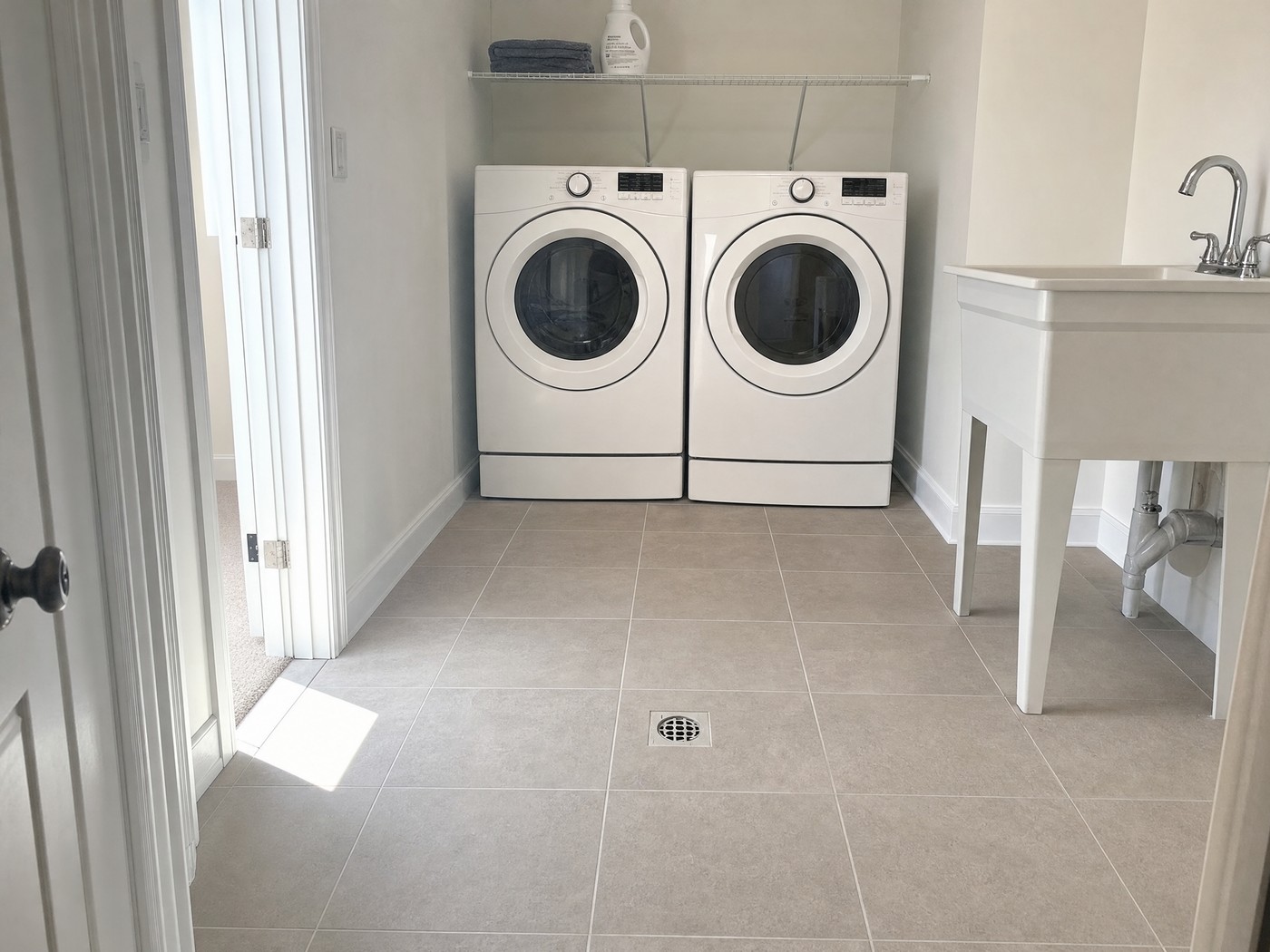 Laundry room floor in greige porcelain tile running under a white washer and dryer, with a flush floor drain