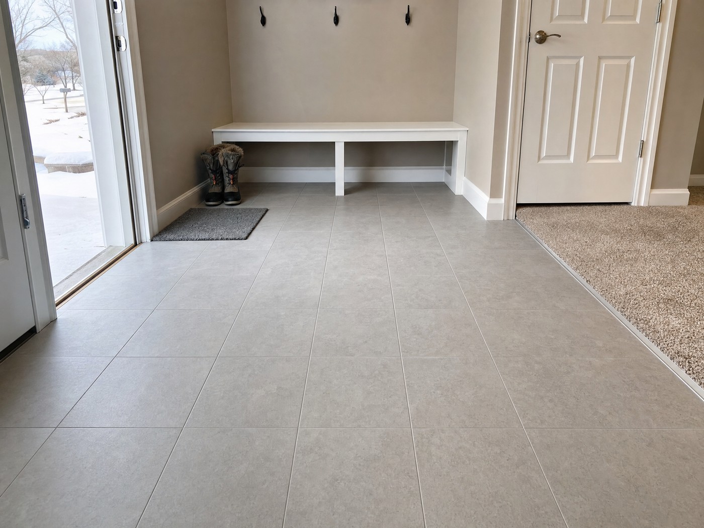 Mudroom entry floor in warm grey porcelain plank tile meeting carpet at a clean metal transition strip